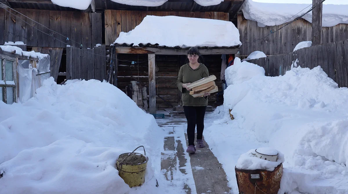 Natalia, the mother of a mobilised soldier, with firewood that her neighbour brings her. <a href="https://www.youtube.com/watch?v=NjrPBmXX3vo" rel="noopener noreferrer" title="https://www.youtube.com/watch?v=NjrPBmXX3vo">A shot from the film “Firewood for the mobilised”</a>