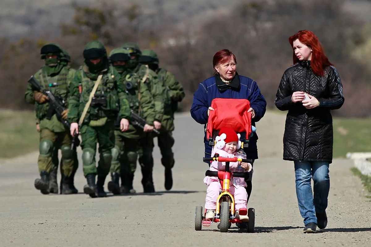 Женщины на фоне вооруженных людей в военной форме без опознавательных знаков за территорией украинской воинской части в селе Перевальное под Симферополем, Украина, 14 марта 2014 года. Фото: Юрий Кочетков / EPA