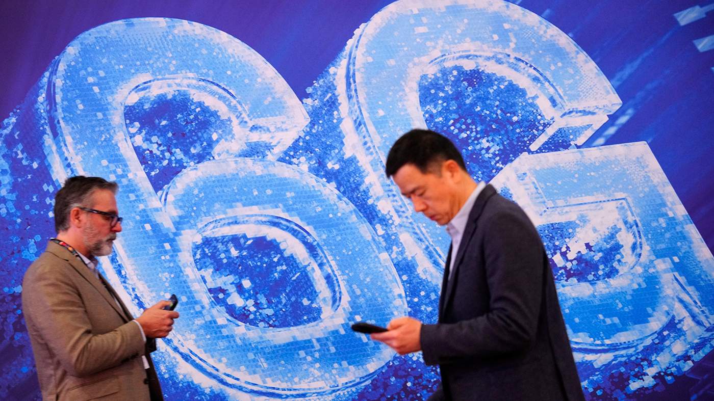 Мужчины проверяют свои мобильные телефоны на фоне экрана с рекламой 6G во время 20-го Всемирного мобильного конгресса (MWC) в Барселоне, Испания. 2 марта 2026 года. Фото: Alejandro Garcia / EPA