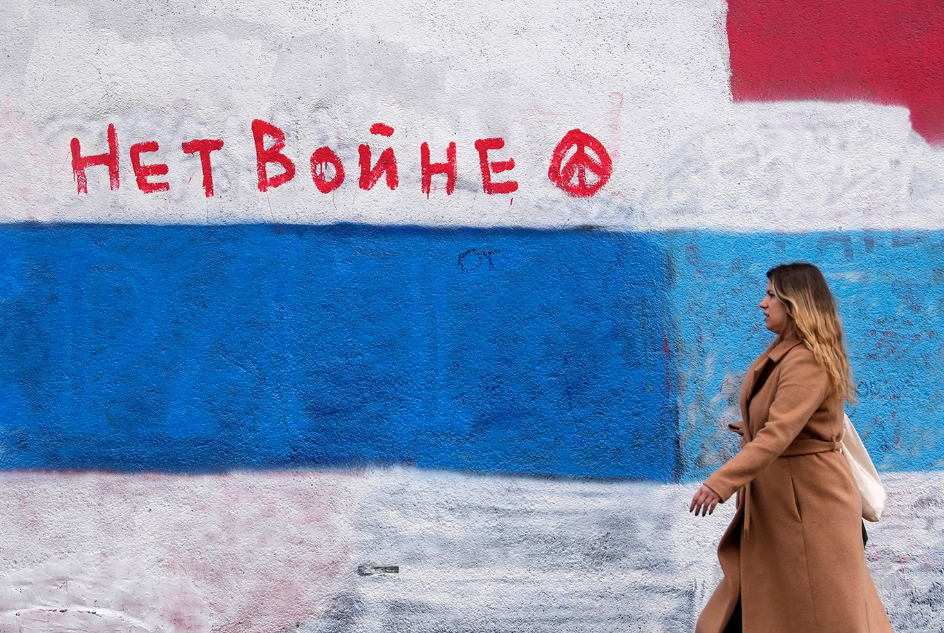 Женщина проходит мимо стены, на которой раньше была фреска с изображением президента России Владимира Путина, с тех пор закрашенная бело-сине-белым флагом, символом оппозиции российскому вторжению в Украину в 2022 году, в Белграде, Сербия, во вторник, 6 декабря 2022 год. Фото: Darko Vojinovic / AP / Scanpix / LETA