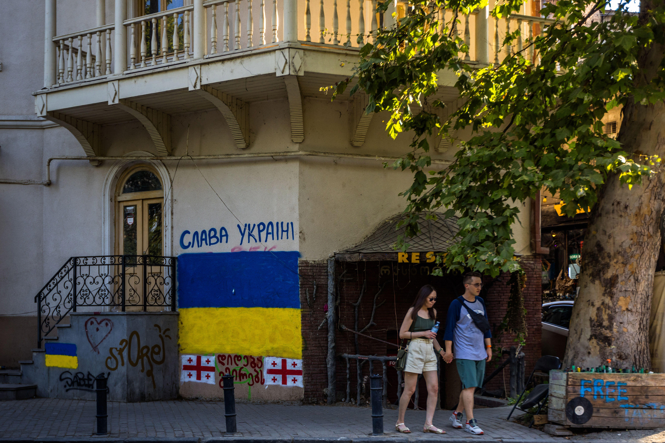 Пара проходит мимо фасада здания с изображением флага Украины. Тбилиси, Грузия. 11 сентября 2023 года. Фото: Georg Berg / Alamy / Scanpix / LETA