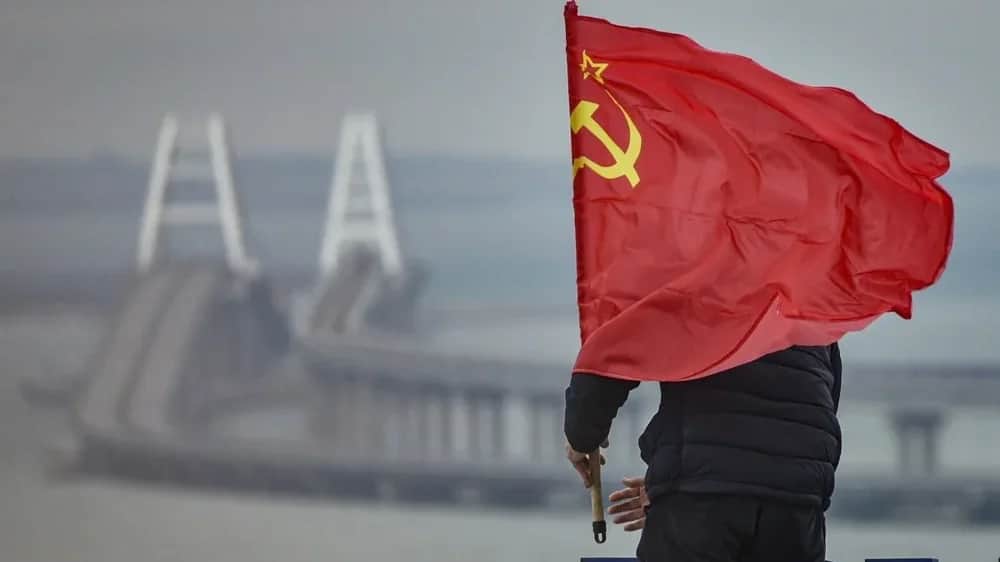 A man mounts a Soviet flag on an observation deck overlooking the Crimean Bridge in Kerch, annexed Crimea, 14 March 2023. Photo: EPA
