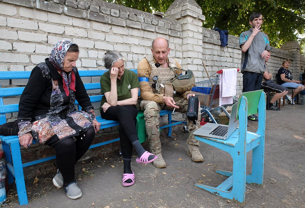 Украинский военнослужащий сидит рядом с местными жителями за ноутбуком в центре города Суджа, Курская область, Россия, 21 августа 2024 года. Фото: EPA-EFE